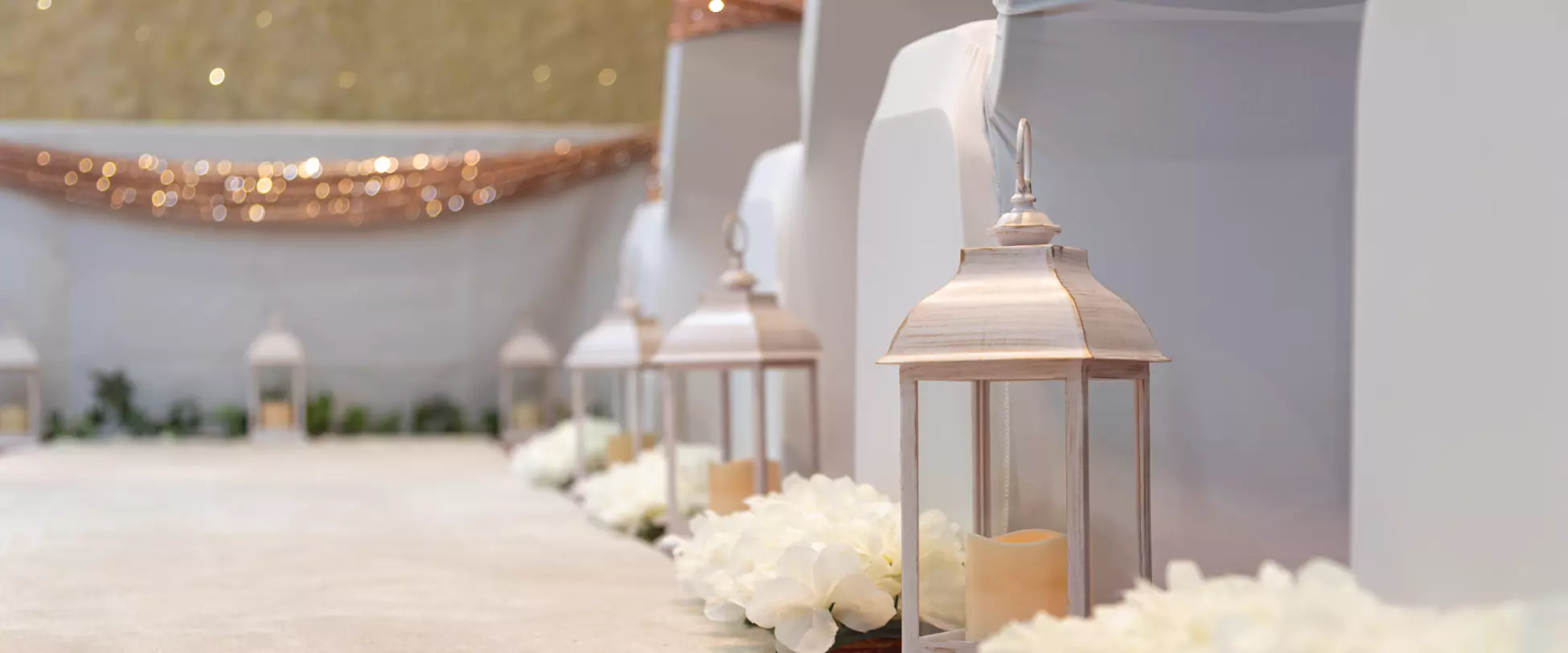 The aisle of a wedding with chairs, lanterns and flowers lining the aisle.